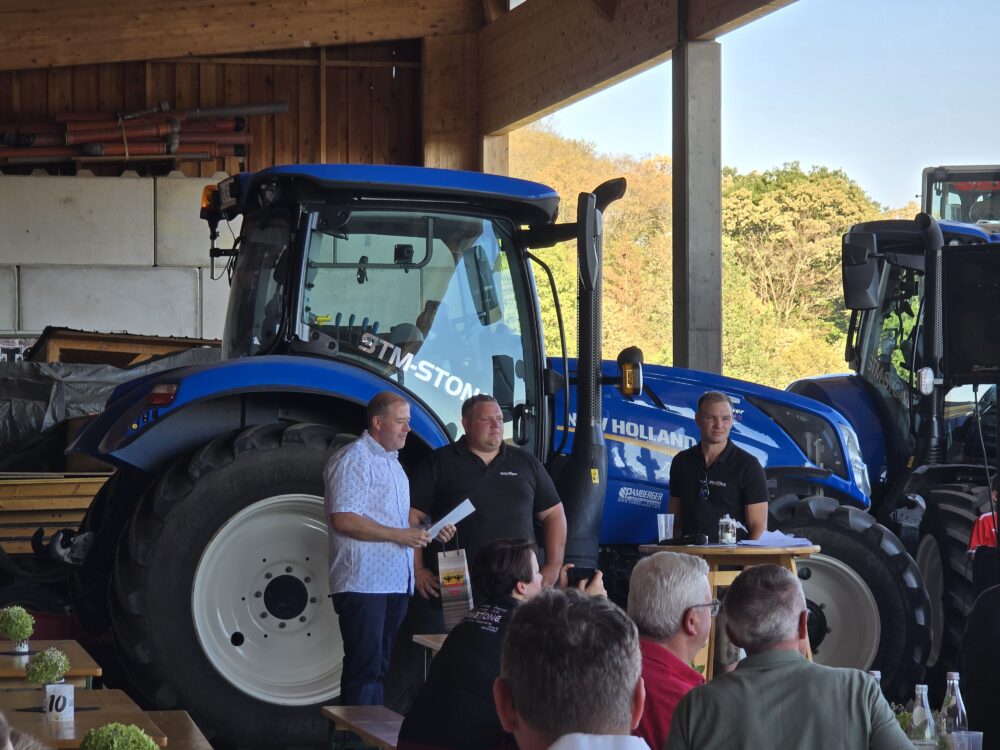 Traktor-Vorführung mit drei Männern im Freien, ein Mann hält Dokumente in der Hand.
